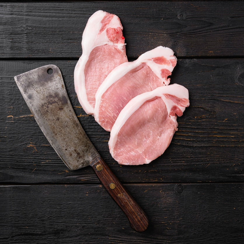 Raw pork steak ready for cooking with herbs, on black wooden table background, top view flat lay, with copy space for text