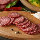 Slices of salami with vegetables pepper and garlic on a cutting board on a wooden table.